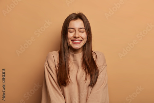 Portrait of beautiful woman with straight dark hair, smiles broadly, keeps ey...