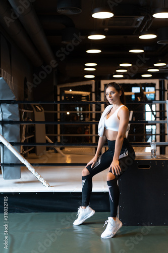 Smiling fit girl holding towel and taking rest in gym.