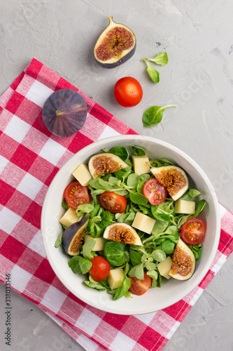 Fresh salad with figs, leaves, cherry tomatoes and cheese on gray background. Free space for text. Top view. Abstract food background with napkin