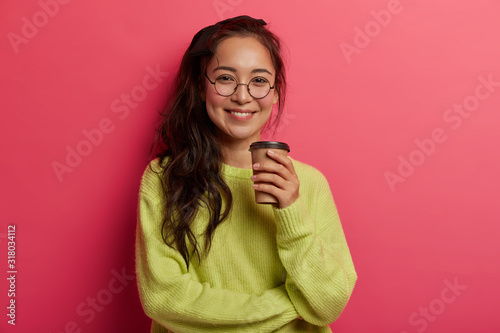 Smiling lovely female model enjoys drinking coffee during spare time, has good mood, casual talk with intelocutor, looks directly at camera, dressed casually, has caffeine addiction. Lifestyle concept