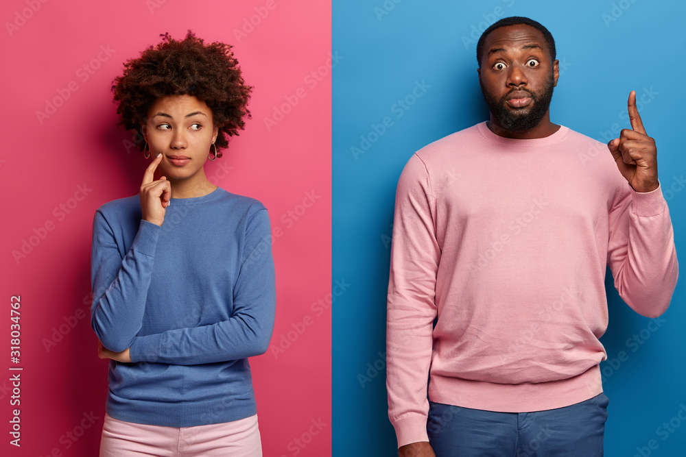 Φωτογραφία Shocked bearded man points index finger above, demonstrates something stunning, thoughtful curly woman stands near, thinks what to choose better