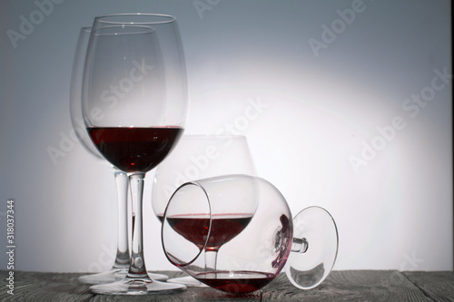 Glasses with red dry wine. One of them lies on its side with the remains of wine. Stand on wooden boards. Shot in backlight.