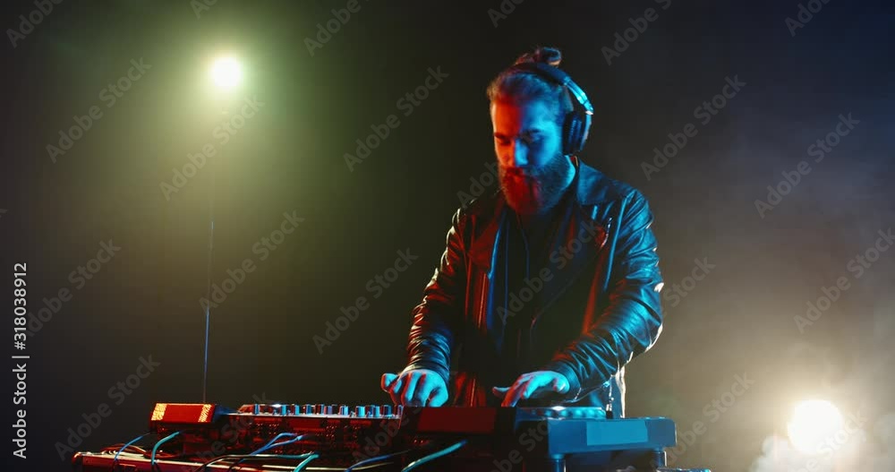 A cool bearded dj standing at the mixer controller, composing a new mix and rocking the party in a nightclub - nightlife concept 4k footage