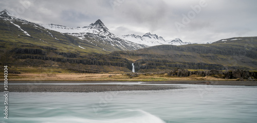 Long exposure shot by the river of Hamersa with snowy mountain peaks, basalt columns and waterfall underneath. From Hamarsdalur near Bragdavellir in east Iceland. Travel and landscape concept. photo