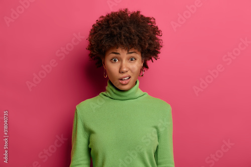 Photo of displeased dark skinned female purses lips, sees something unpleasant, unwills giving answer on tricky question, has talk with friend, discuss not interesting information, wears green clothes © wayhome.studio 