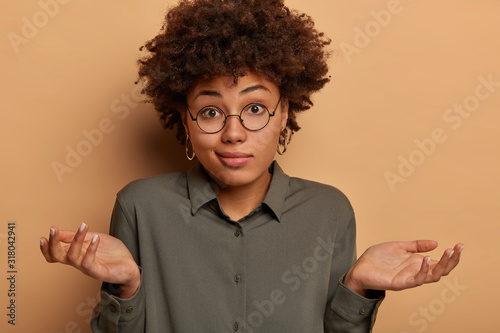 Foto Careless hesitant woman shrugs shoulders, spreads arms sideways, cant help or ha