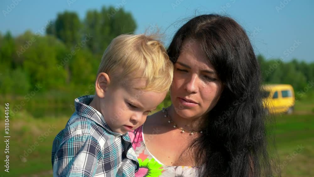 Happy Young Mother Hugging And Kissing Cute Child Holding On Hands. Summer River Lake Morning Sunny Day Blue Sky. Slow motion 30p 0.5 60p Happy Young Mother Hugging And Kissing Cute Child Holding On Hands. Summer River Lake Morning Sunny Day Blue Sky. Slow motion 30p 0.5 60p