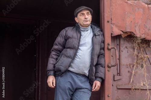 Middle Age Man Leaning on Open Door of Old Abandoned Railway Wagon and Looking Into The Distance