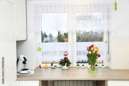 Klorowe tulipany w wazonie na parapecie białego wspłóczesnego okna w jasnej kuchni.