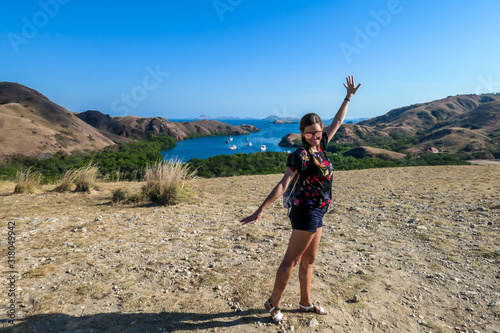A girl standing on top of the Komodo Island in Indonesia. The girl is having a lot of fun, enjoying her time. Happiness and fun while travelling. Discovering new places. There is a lot of boats photo