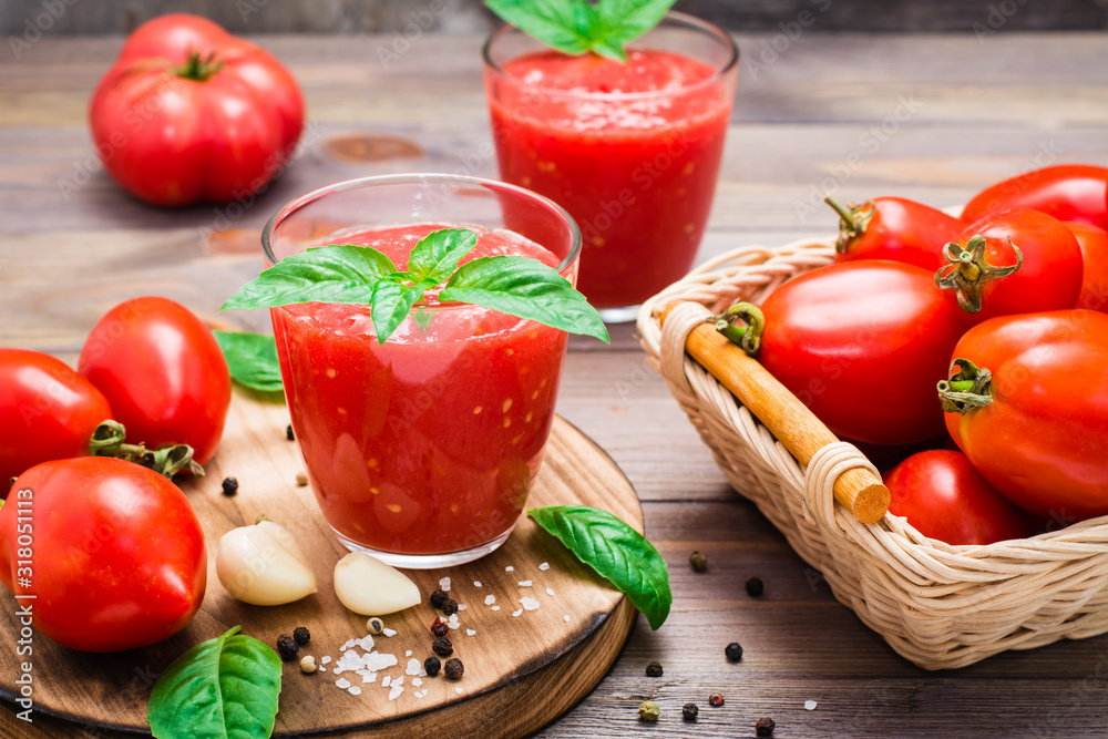 Appetizing fresh tomato juice with basil leaves in glasses and ingredients for its preparation on a wooden table Appetizing fresh tomato juice with basil leaves in glasses and ingredients for its preparation on a wooden table