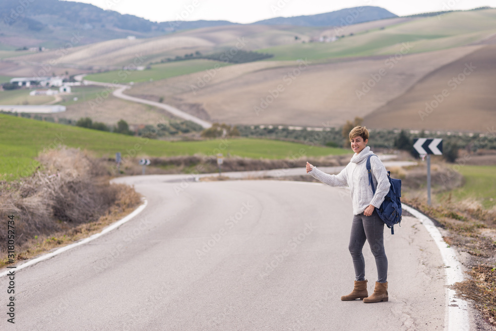 Obraz premium Woman with backpack hitchhiking on a lonely rural road.