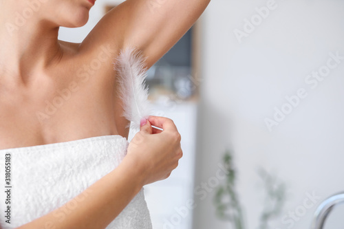 Beautiful young woman with feather in bathroom, closeup. Concept of using deodorant photo