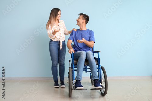 Handicapped young man in wheelchair and his wife near color wall