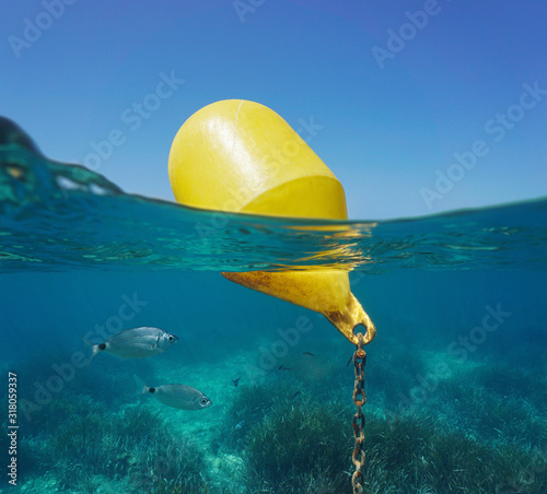 A yellow beacon buoy in the sea for beach marking and cross channel limits with blue sky and fish underwater, split view half over and under water surface, Mediterranean, Spain photo