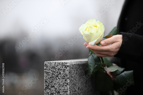 Photo Woman holding white rose near grey granite tombstone outdoors, closeup