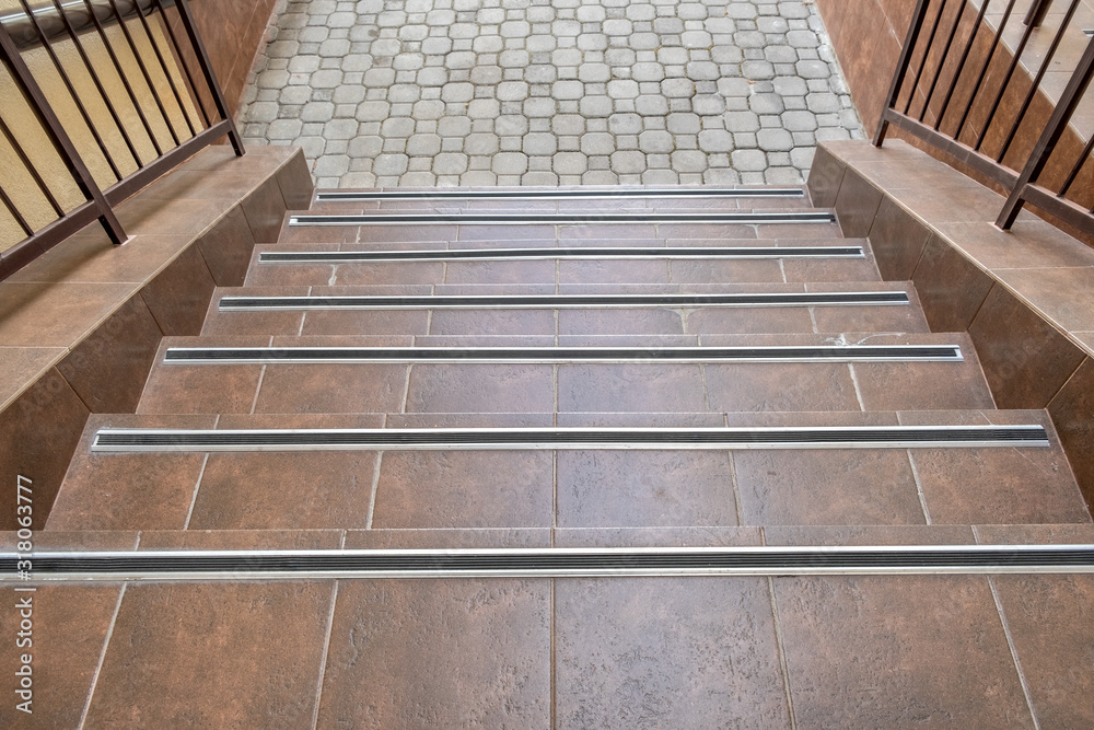 Concrete entrance stairs covered with ceramic tiles with metal railings