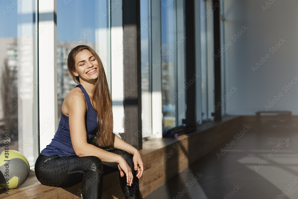 Sport makes me happy. Lifestyle and gym concept. Cheerful attractive woman, fitness instructor start morning with exercise in fitness club, sitting near window with medicine ball, smiling teeth