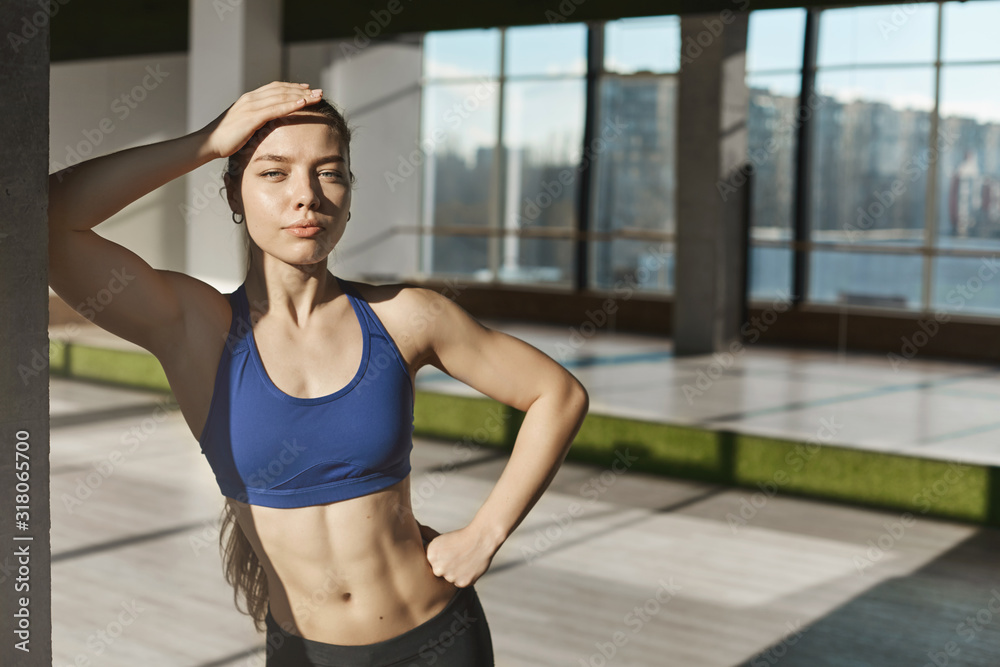 Athletic and strong good-looking young fitness instructor, sportswomen in sportsbra, showing six-pack perfect body, leaning on wall in gym, dance studio, mirrors behind, looking camera confident Athletic and strong good-looking young fitness instructor, sportswomen in sportsbra, showing six-pack perfect body, leaning on wall in gym, dance studio, mirrors behind, looking camera confident