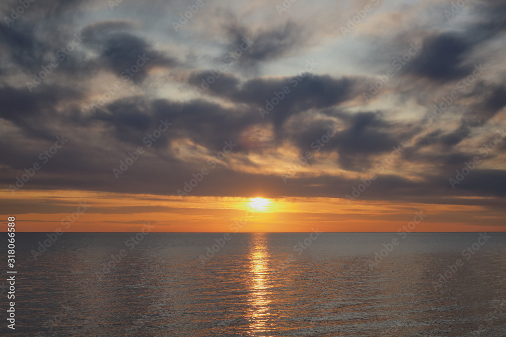 Golden sunset with lots of clouds above water horizon.