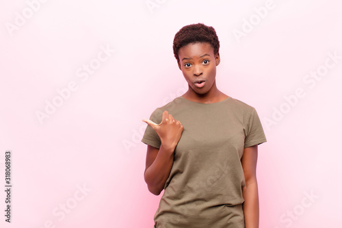 young pretty black womanlooking astonished in disbelief, pointing at object on the side and saying wow, unbelievable against pink wall photo