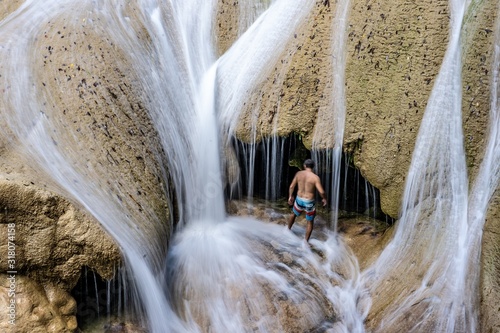 Man standing in shorts in a cave with water pouring down during the daytime photo