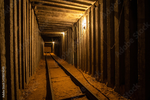 Empty underground square tunnel with rails for minecart and warm tungsten lighting. 