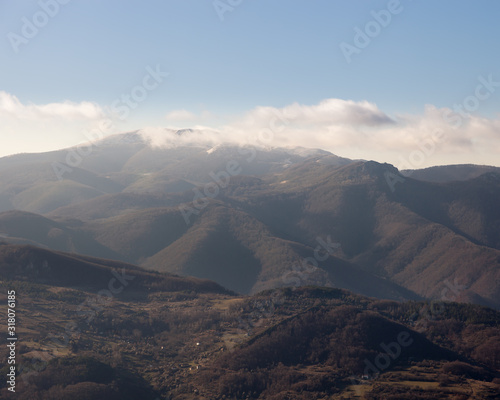 Distant mountain peak covered by clouds and fog, beautiful sunlit highlands and clear blue sky