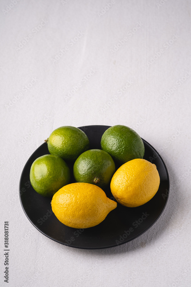 Lime and lemon sour fruits in black plate on white background, angle view, vitamins and healthy food Lime and lemon sour fruits in black plate on white background, angle view, vitamins and healthy food