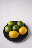 Lime and lemon sour fruits in black plate on white background, angle view, vitamins and healthy food