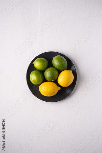 Lime and lemon sour fruits in black plate on white background, top view, vitamins and healthy food