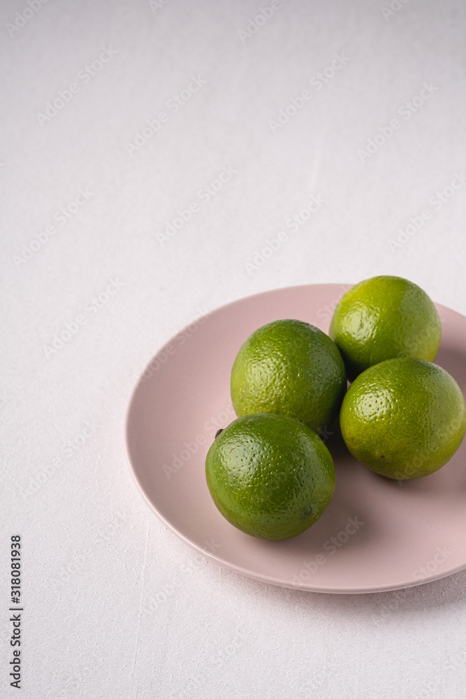 Lime sour fruits in pink plate on white background, angle view, vitamins and healthy food Lime sour fruits in pink plate on white background, angle view, vitamins and healthy food