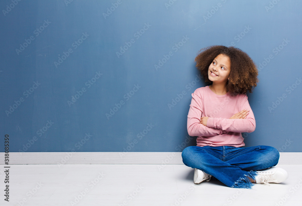 african american little girl feeling happy, proud and hopeful, wondering or thinking, looking up to copy space with crossed arms sitting on the floor - obrazy, fototapety, plakaty 