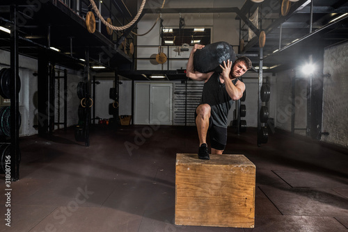 Принти на полотні Young strong sweaty fit muscular man with big muscles holding heavy sandbag on h