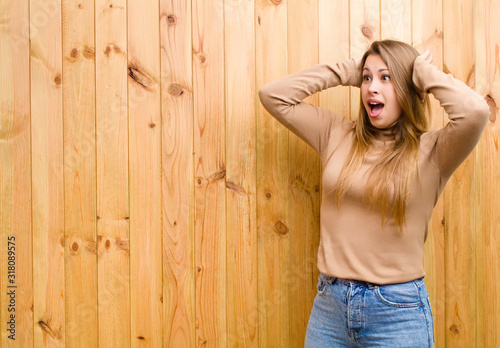 young blonde woman with open mouth, looking horrified and shocked because of a terrible mistake, raising hands to head photo