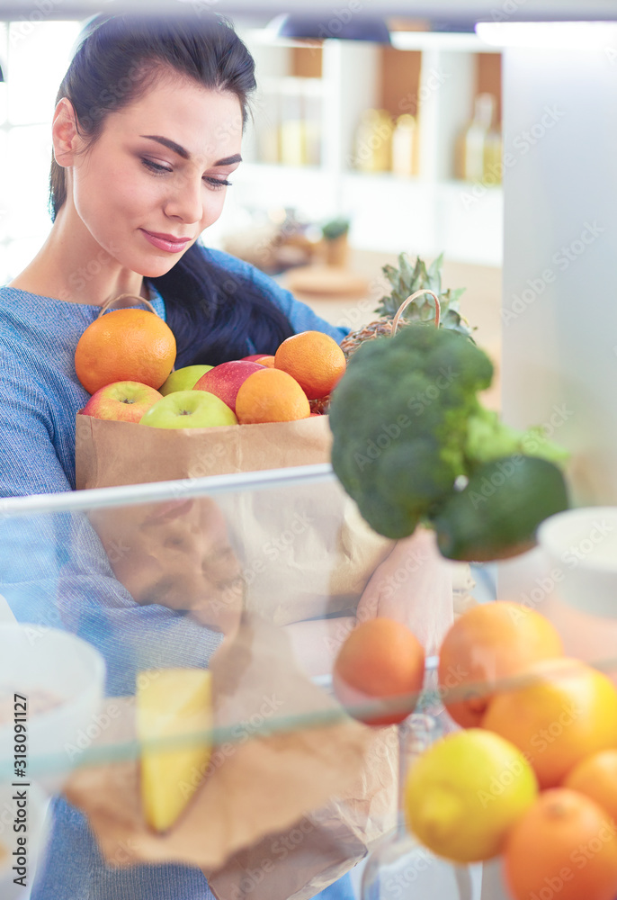 Smiling woman taking a fresh fruit out of the fridge, healthy food concept