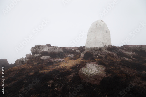 White mountain peak stone, dark, burned grass after a fire, orange rocks covered by moss and thick mist