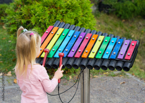 Fotografie Beautiful little girl plays on a multi-colored xylophone in a park