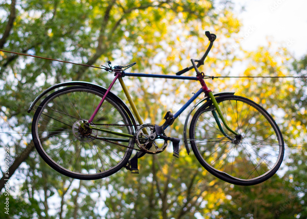 Fototapeta premium Multi-colored bicycle hanging in the air among the trees in the park