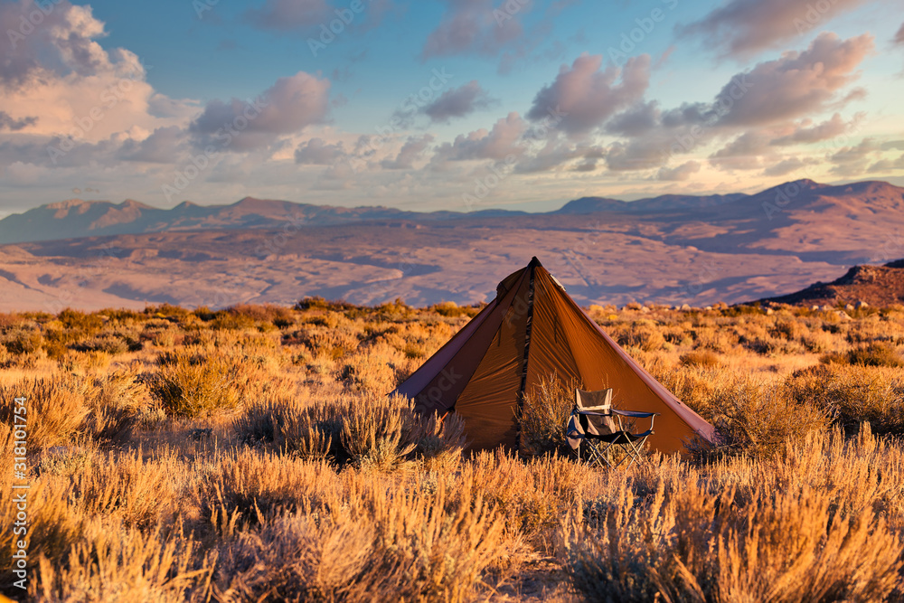 Indian style tipi tent with folding camp chair nearby pitched in the desert under the mountains of the Sierra Nevada