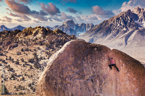 Man rock climbs on huge granite boulder in the Buttermilk area of Bishop, California with the Sierra Nevada  behind photo
