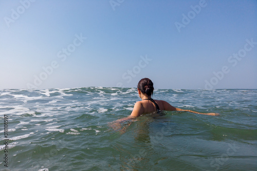 Young woman in black swimsuit spends time in sea. Adult lady swims towards the waves.