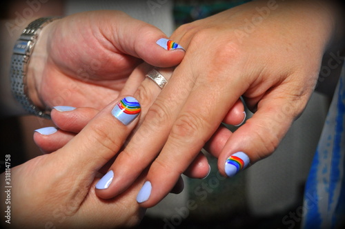 Close up of two hands holding with their nails painted with rainbow