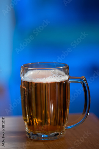 A glass of beer on a wooden table and blue background viewed from the side