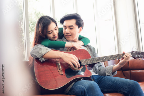 Young Couple Love Having Fun While Sing a Song and Playing Guitar in Living Room Together, Portrait of Couple are Relaxing at Their Home. Romantic Lifestyles an Valentine's Day Concept