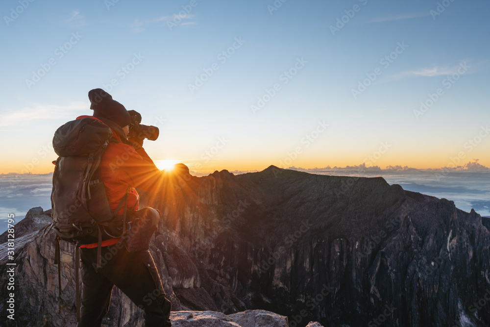 a man with backpack taking photo over the clouds in sunrise moment on Kota Kinabalu summit in Malaysia. Travel lifestyle and adventure concept - obrazy, fototapety, plakaty 