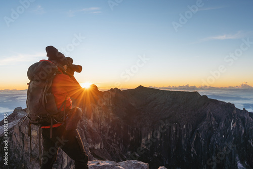 a man with backpack taking photo over the clouds in sunrise moment on Kota Kinabalu summit in Malaysia. Travel lifestyle and adventure concept photo