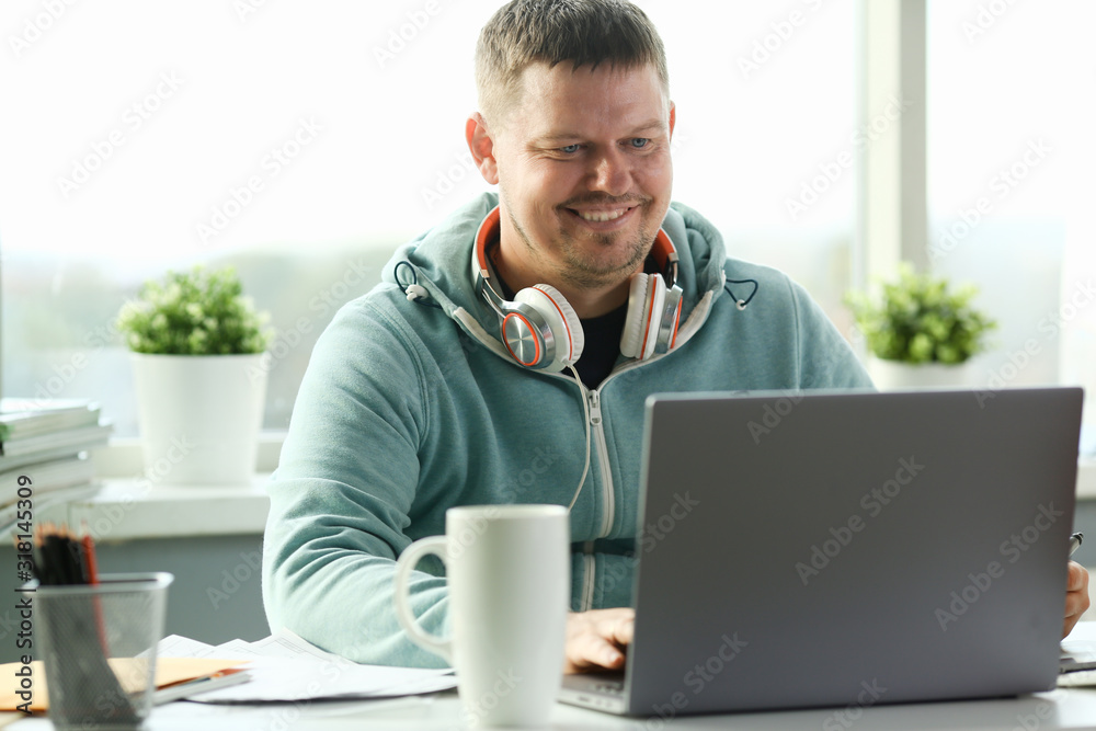Handsome smiling male student using online education service. Young man looking in laptop display watching training course and listening it with headphones. Modern study technology concept