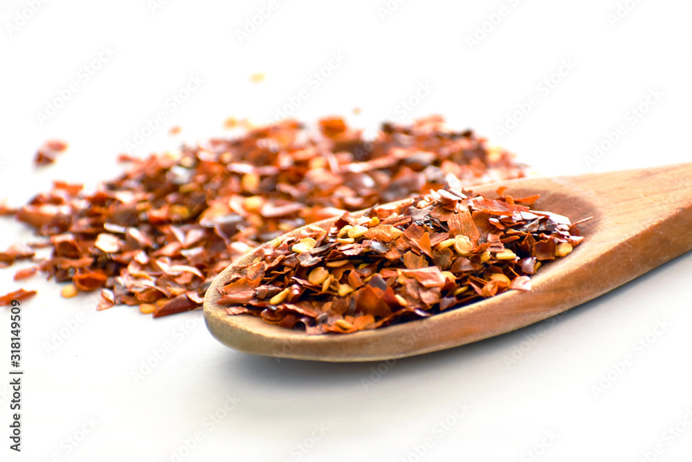 Dried chilli flakes or crush red pepper on a wooden spoon on white background with copy space on the left side. Selective focus. Dried chilli flakes or crush red pepper on a wooden spoon on white background with copy space on the left side. Selective focus.