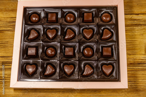 Assorted chocolate candies in a box on wooden table. Top view